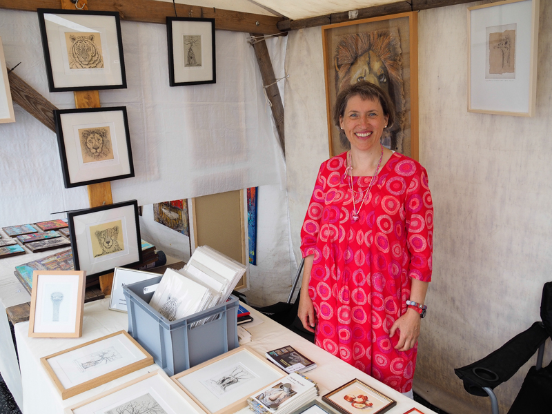 Das Bild zeigt die Künstlerin Heike Pander in ihrem Verkaufsstand vor ihren Radierungen während der Open Air Gallery auf der Oberbaumbrücke in Berlin (2019).